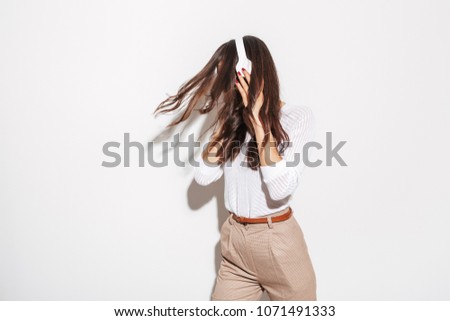 Portrait of a young asian businesswoman listening to music with headphones and dancing isolated over white background