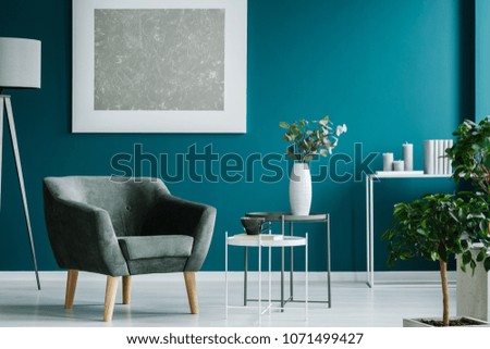 Green armchair against blue wall with silver painting in living room interior with plants Royalty-Free Stock Photo #1071499427