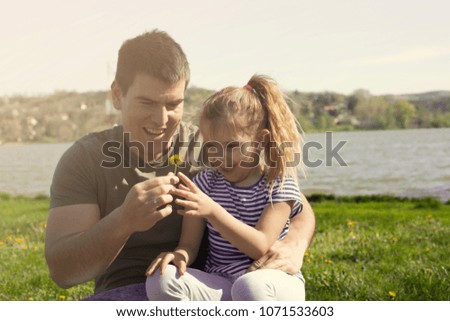 Father and daughter sitting next to river,holding flower.