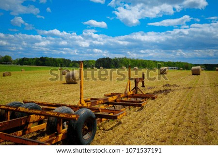 A hay trailer in a field of freshly baled hay in North Carolina. Blue sky speckled with low cumulus clouds.