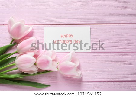 Tulips and greeting card with phrase "Happy Mother's Day" on wooden background