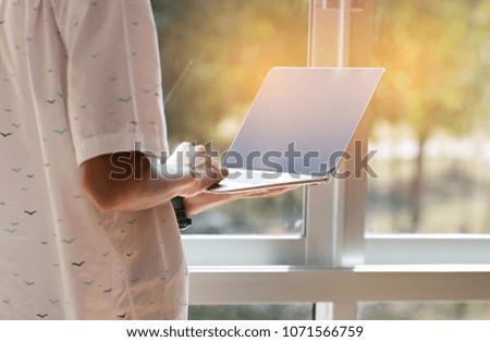 Online searching social networks by Smartphone Concept: Businessman stand using laptop computer device, hands typing text message to connect wifi for shopping online in office window.