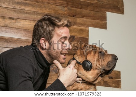 Dog with music headphones, and a guy playing with it. Funny picture with a Sharpei dog