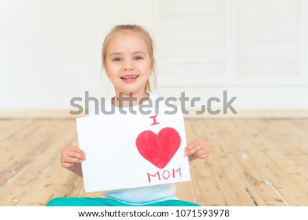 Little girl paints greeting card for Mom on Mother's Day with the inscription I love you mom . Indoors. Mother's Day concept.