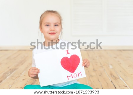 Little girl paints greeting card for Mom on Mother's Day with the inscription I love you mom . Indoors. Mother's Day concept.