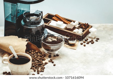 Variety things for prepare coffee. Roasted beans, ground coffee, scoop, electric coffee machine and assortment of sweets and spices to eat with on light background.