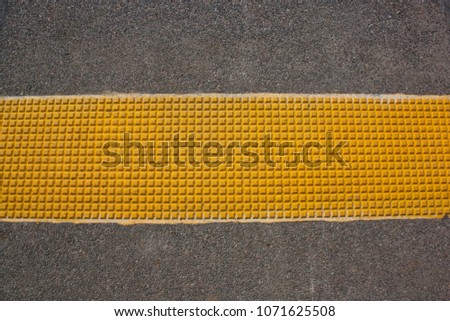 Asphalt with yellow tactile paving slab.