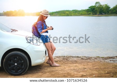 woman of traveler standing near the car and looking at the picture on camera near the lake background is mountain during holiday.Young lady tourist enjoying on vacation. 