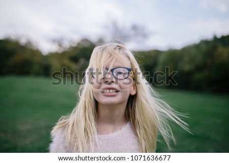 portrait of smiling disheveled blonde girl with glasses outdoors in park