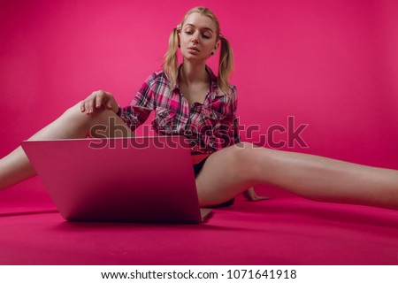 Happy young woman or teenager sitting on the floor with crossed legs and using laptop on pink