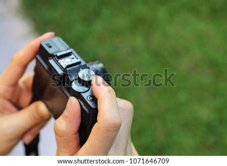 Closeup of a small black compact camera carried by woman's hands with green blackground.