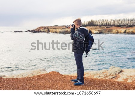 Young photographer with backpack making photos of sea and rocks with the camera. Mediterranean sea