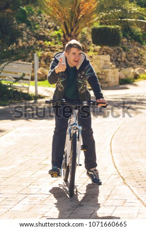 Handsome young man with bicycle showing thumbs up in park on sunny day