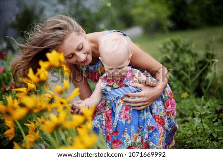 Family. Portrait of beautiful cheerful mother with her cute daugher having fun together in the garden. Smiling girl with yellow flowers