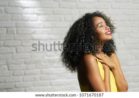 Portrait of happy latina woman smiling and saying prayer. Black girl looking up while praying. Royalty-Free Stock Photo #1071670187