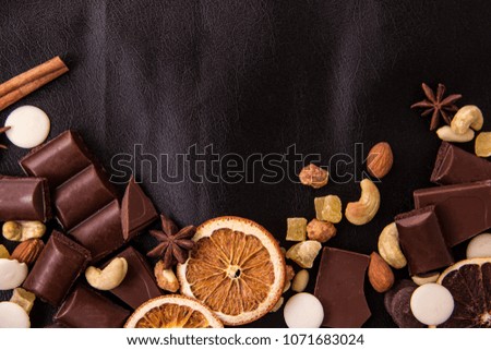 Broken chocolate pieces, nuts, marzipan and dried grapefruit lie on black leather with space for text
