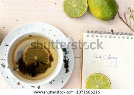 Good morning theme, very green color. Pretty card with cup of aromatic green tea, lime and apples on white wooden background and simple notedook with handwritten text. Romantic view