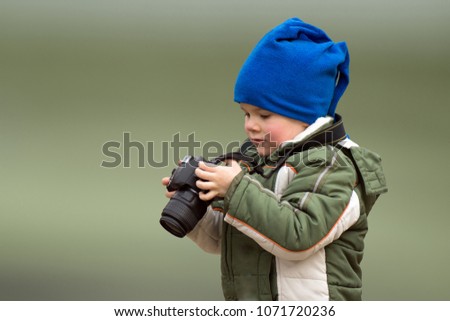 The little boy photographer is holding in hands a camera on green background.