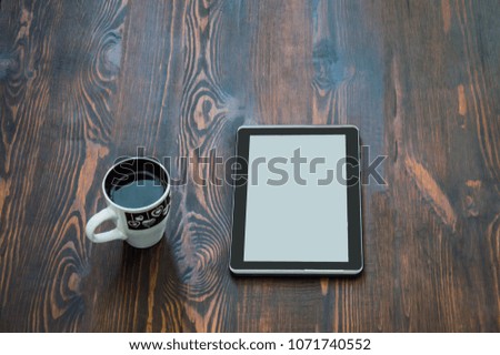 black tablet and a cup of coffee lie on a wooden brown floor or table, view from the top