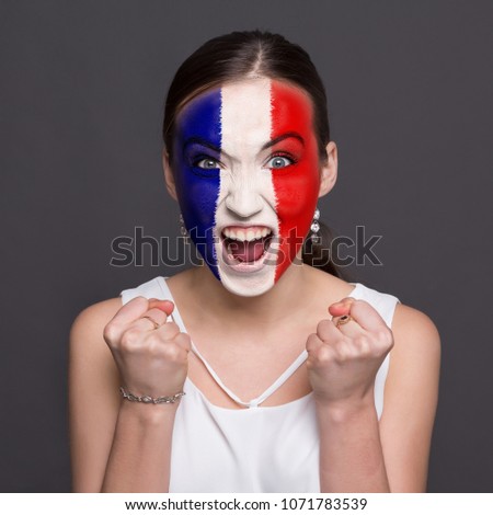 Face of young happy woman painted with flag of France. Football or soccer team fan, sport event, faceart and patriotism concept. Studio shot at gray background, copy space