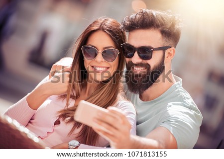 Happy young couple taking selfie with phone on street.