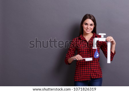 A woman holds an image of a faucet with a drop of water on a gray background. Hygiene concept.