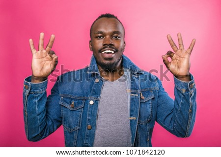 African gesticulates with his fingers okay standing on a pink background