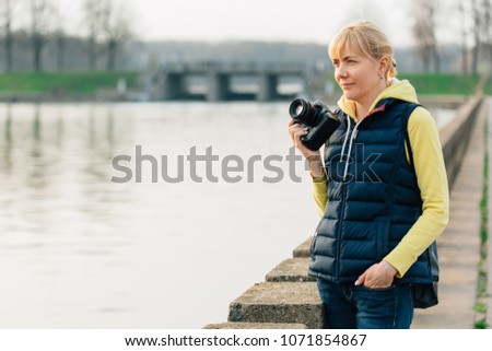 Girl with professional camera in hands. Close up of female photographer in park.