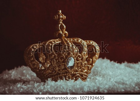 Gold and very expencive gold crown on snow and blur background of red wall. Gold crown on white carpet and red background. Vintage photo