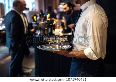 Waiter from catering service carrying champagne wine drinks on the event
