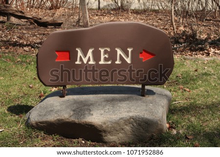Sign outdoors that says, MEN, with a red arrow pointing to the right.                                