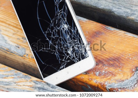 Smartphone with broken display screen is lying on the wooden bench. Closeup, selective focus