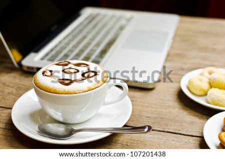 Coffee cup and laptop on the wood texture, selective focus on coffee cream.
