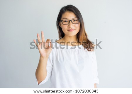 Content pretty Asian girl with highlighted hair making ok sign as symbol of approval. Confident attractive young woman in eyeglasses looking at camera. Student concept