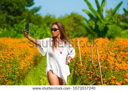 happy and beautiful young Asian tourist woman taking selfie pic in gorgeous orange marigold flowers field natural landscape in travel destination and holidays Summer trip tropical excursion