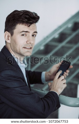 Portrait of confused young manager with phone in office stairwell. Mobile businessman standing on stairwell. Business concept