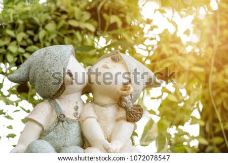 Statue of young boy and girl sitting on timber kissing in beautiful garden.