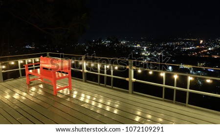 A red armchair on the patio adorned with lamps for a high view of the city at night. Royalty-Free Stock Photo #1072109291