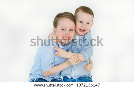 Portrait of two happy and cheerful mast boys in shirts, laughing looking cartoon on the screen and hugging each other, isolated on white background. Friendly brothers. Positive childhood. Friendship.