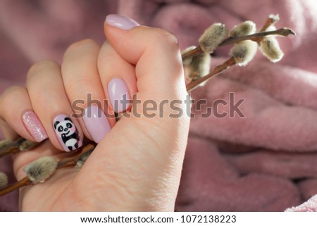Nails with pastel color and a picture of a cute panda. In the hand with manicure - a real branch with fluffy buds.