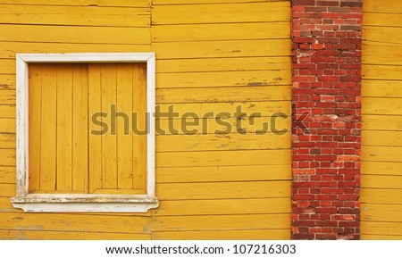 Yellow wooden wall, a closed window and red brick pillar