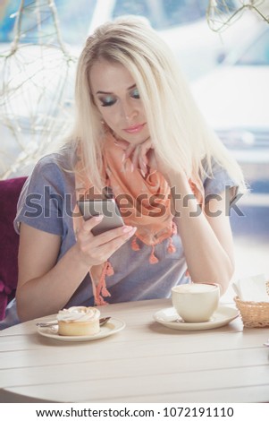 Beautiful woman in the cafe with a cup of cappuccino and a piece of dessert on the plate, soft focus background