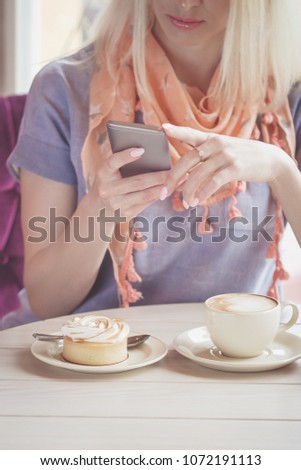 Woman in the cafe with a cup of cappuccino and a piece of dessert on the plate, soft focus background