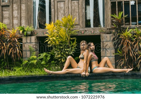 beautiful young women in swimwear resting near swimming pool and looking at camera