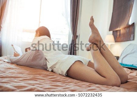 Asian girl who just wake up in the morning. She opened the window to receive the light of the morning sun and reading the magazine or book on her bed.