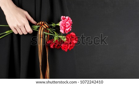 A woman holding a bouquet of red carnations with St. George ribbon at Victory Day celebrations. On black background, copy space, close up