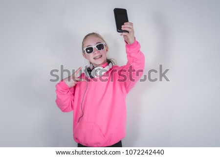 Happy teenage girl taking a selfie/photo with her phone while wearing headphones around neck.