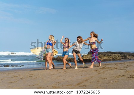 group of beautiful young women walking by seashore with surfboard