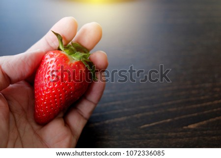 Fresh strawberry in hand with black wood background.