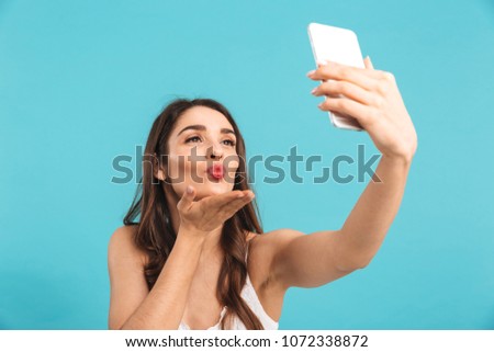 Portrait of a smiling young girl in summer dress taking selfie isolated over blue background
